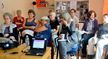 A group of women enjoying a workshop discussion; display board of  WLMA items in background.